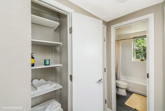 a bathroom with a white door and a white toilet next to a white shelf with white towels